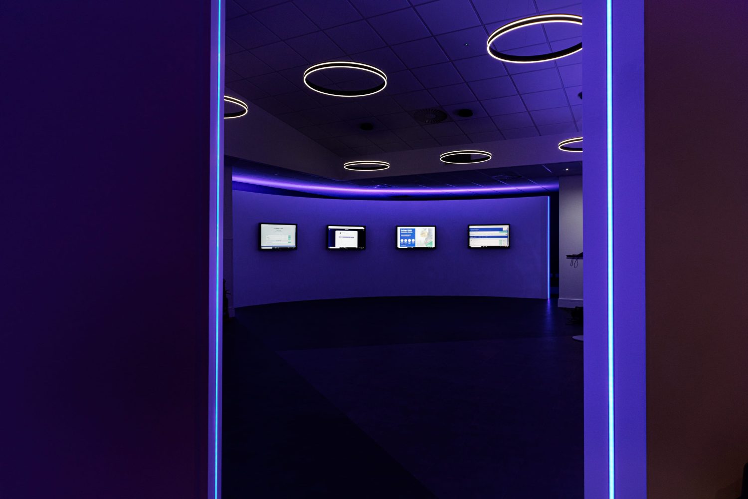 Curved wall with four TVs mounted and purple LEDs glowing around and circular pendant lights hanging from ceiling