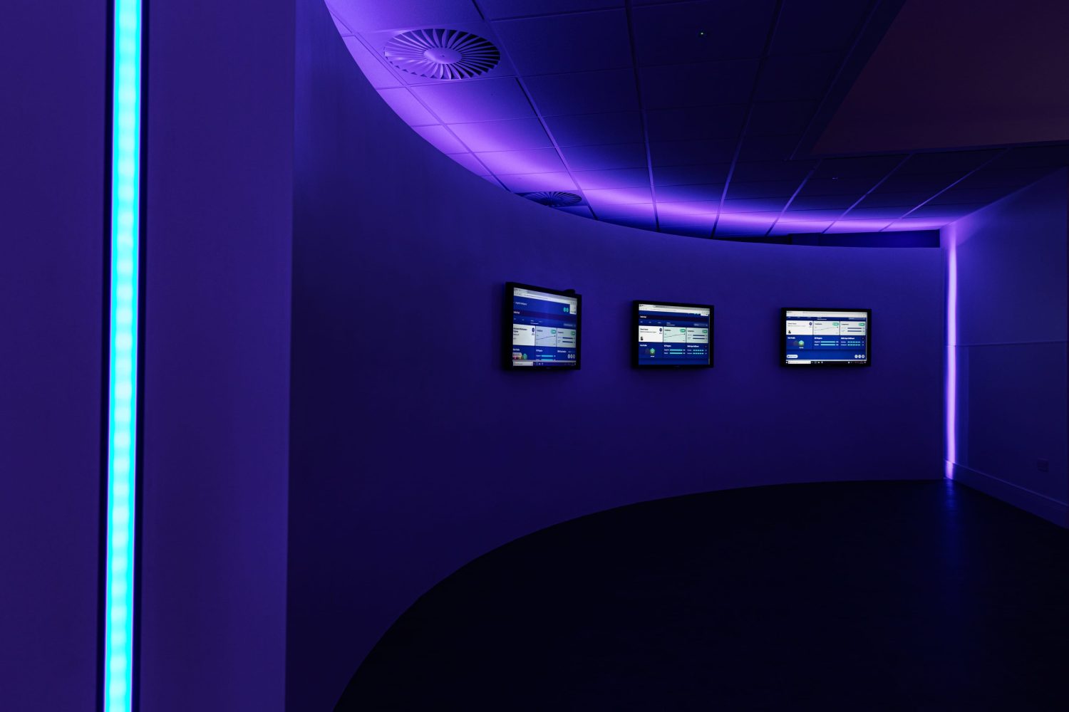 Curved wall with three TVs mounted and purple LEDs glowing around wall