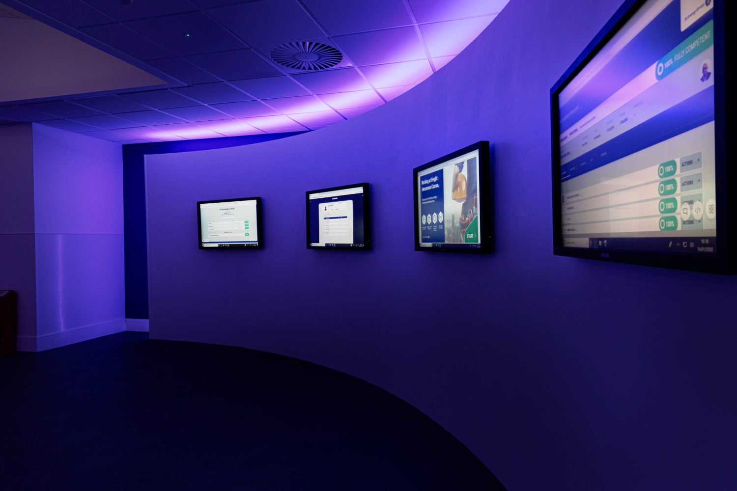 Four TVs mounted to curved wall with purple LEDs glowing around
