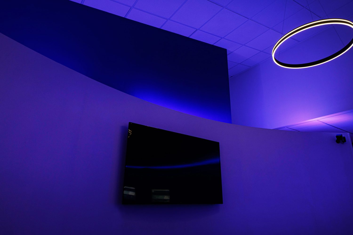 TV mounted to curved wall with purple LEDs glowing around and circular pendant light hanging from ceiling