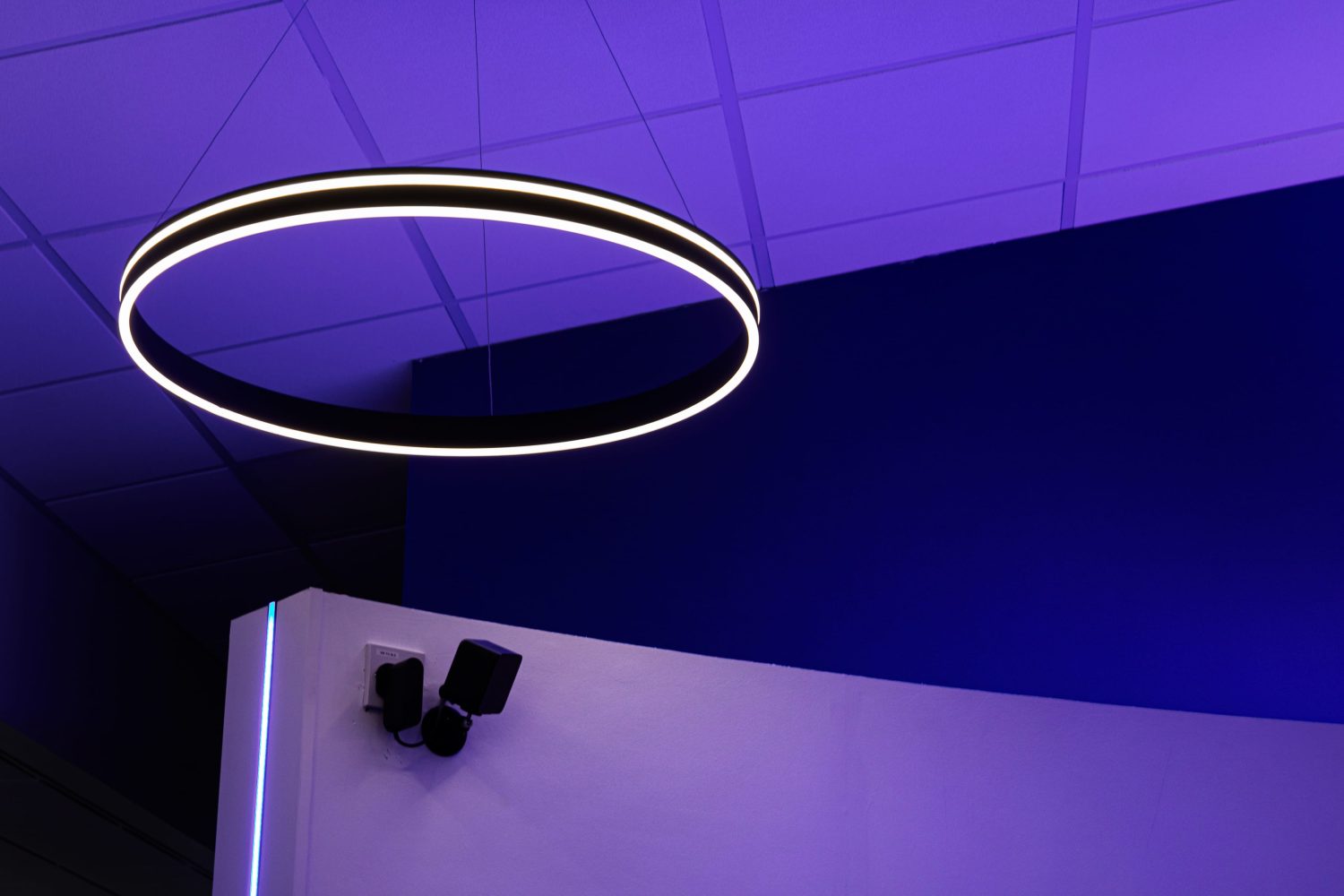 Circular pendant light with two white strips of light going around hanging above curved wall