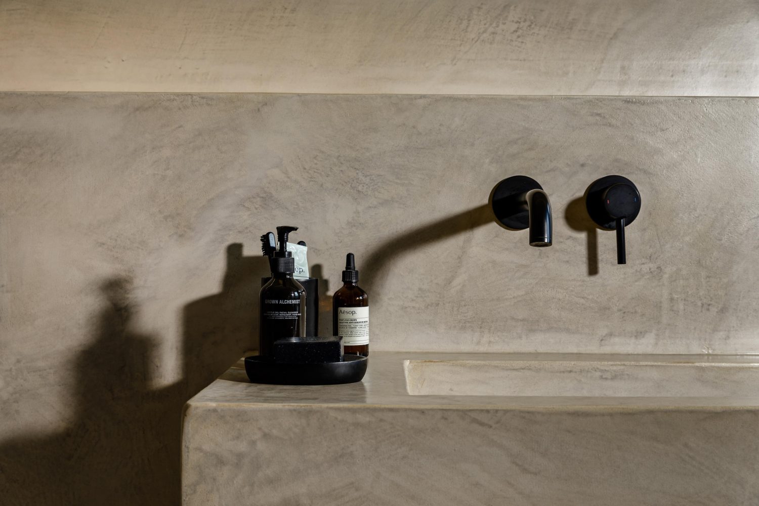 Beige stone sink built into wall with black tap and faucet and soap on counter