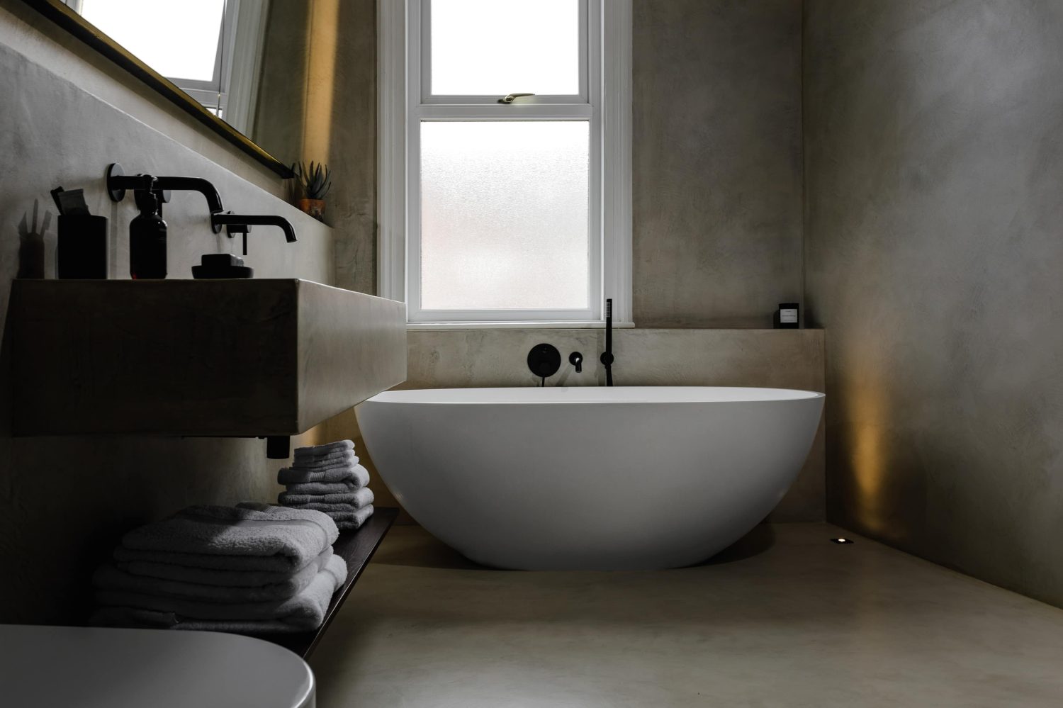 Bathroom with beige stone walls and a large white bath with white framed window on the wall above
