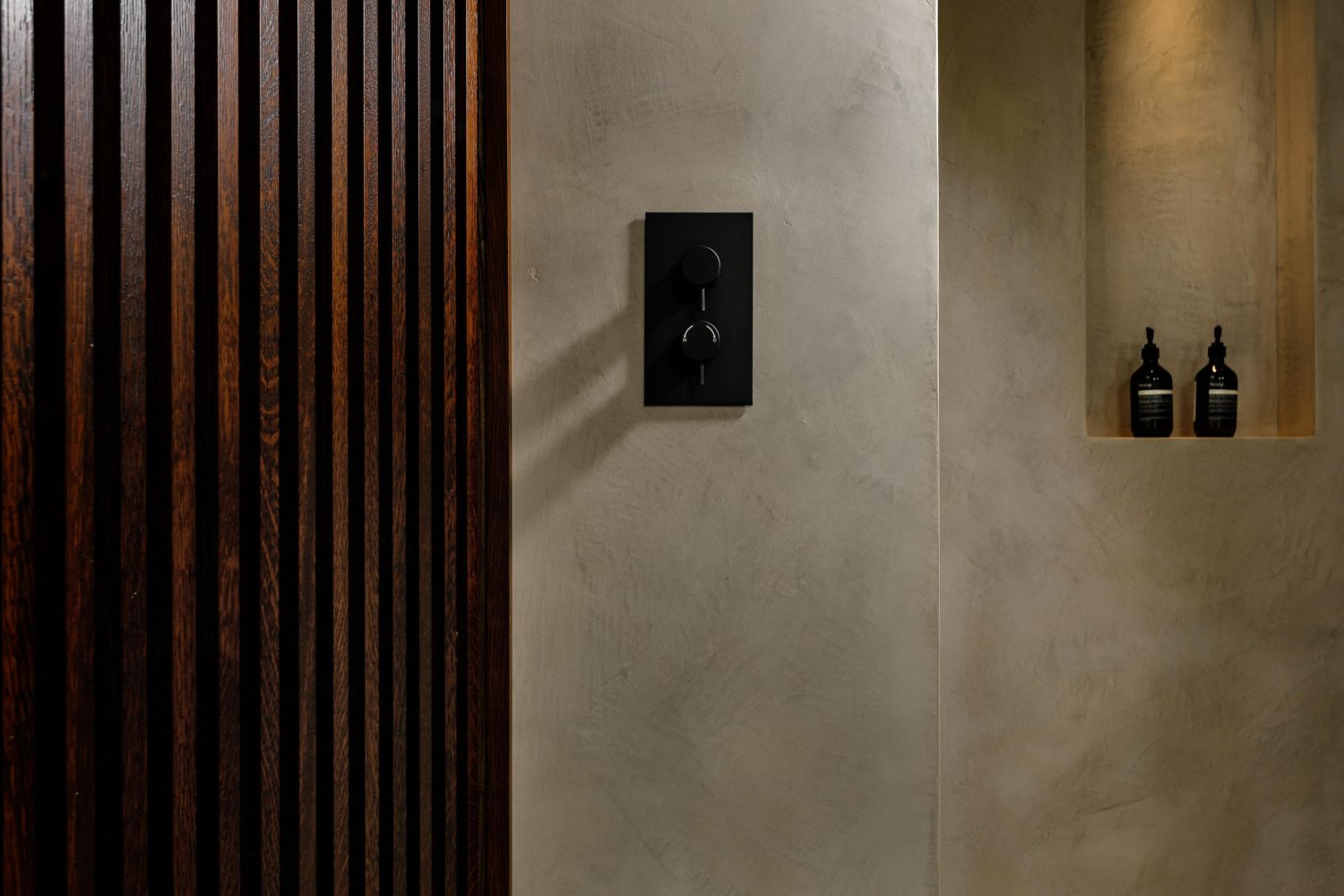 Black buttons on a beige stone textured wall with a shower niche on the wall behind and dark wooden panels to the left