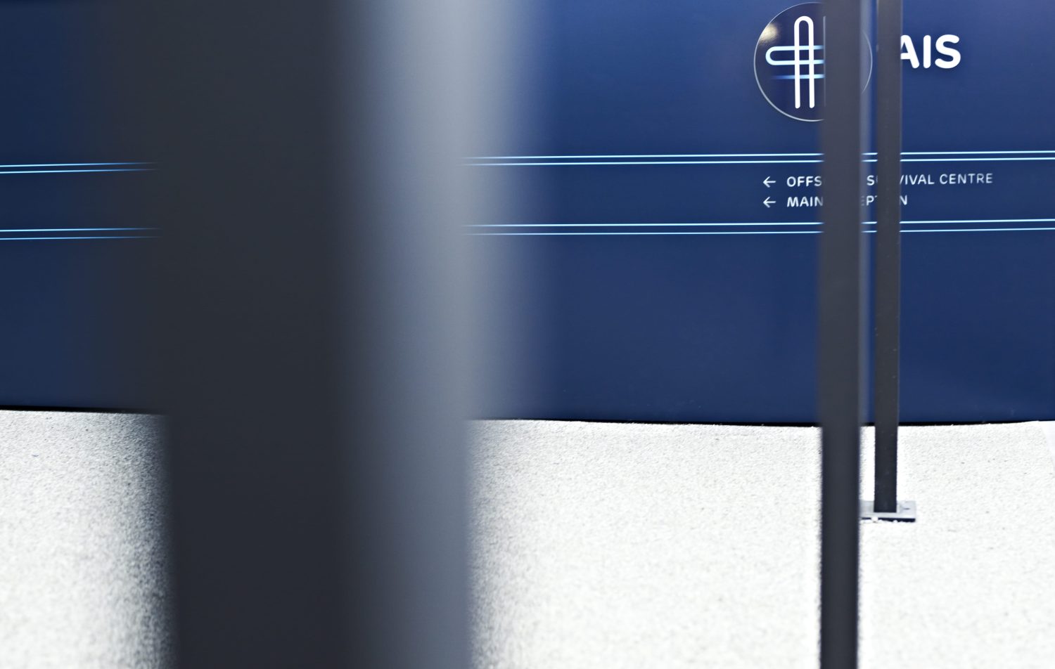 Three black metal poles in front of blue wall with a graphic of company logo on