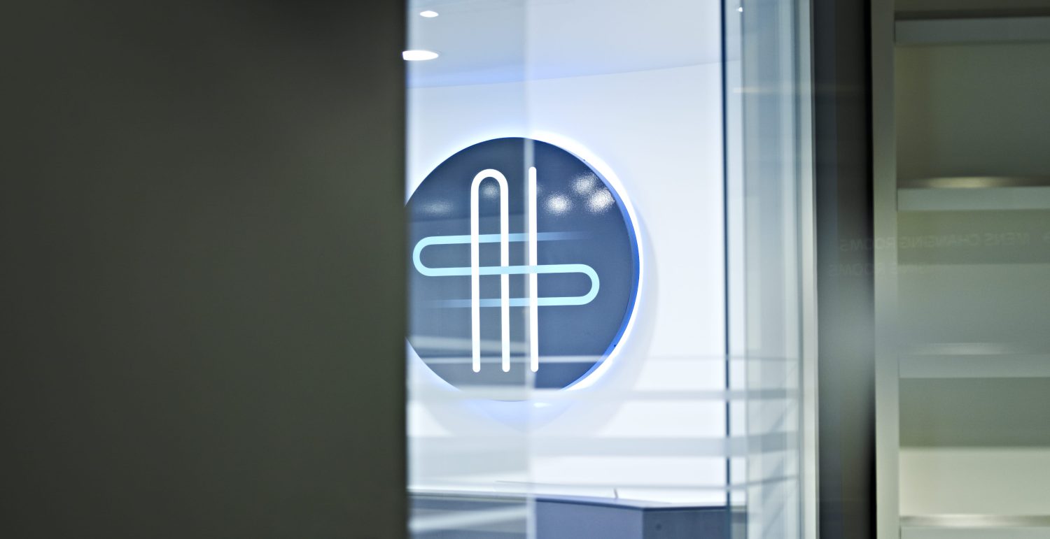 Blue, circular company signage on a white wall viewed through a window