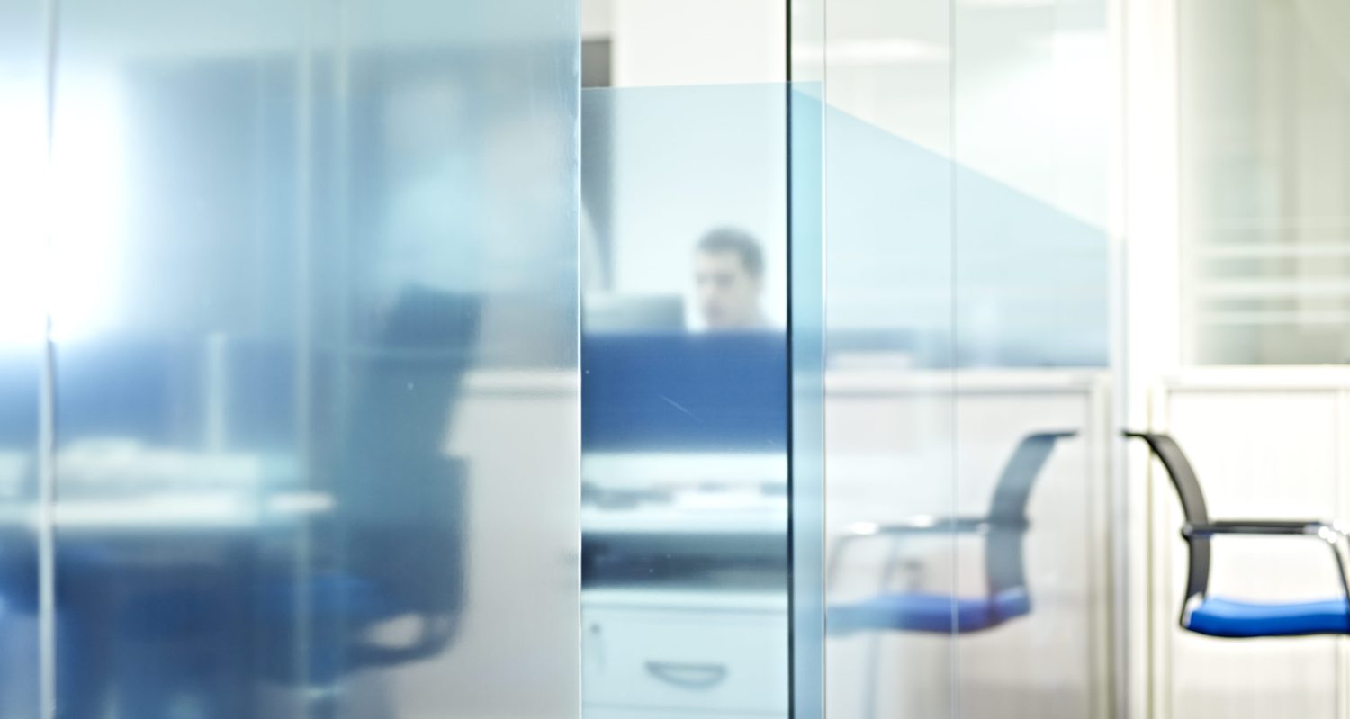 Reflection of an office workspace in a blue tinted glass wall