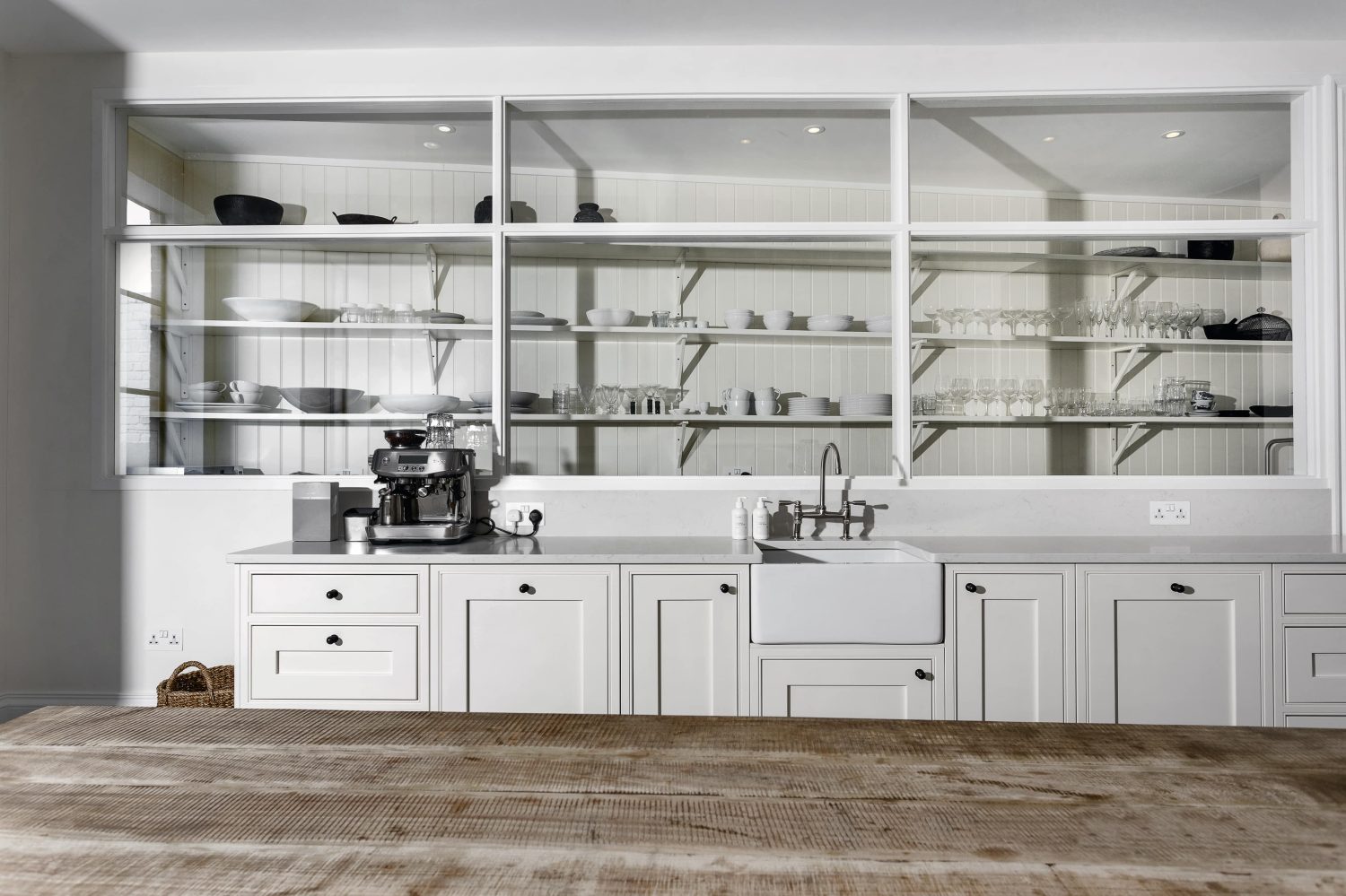 Kitchen with white built-in shelving along a wall with white cabinets beneath featuring a white sink and silver coffee machine