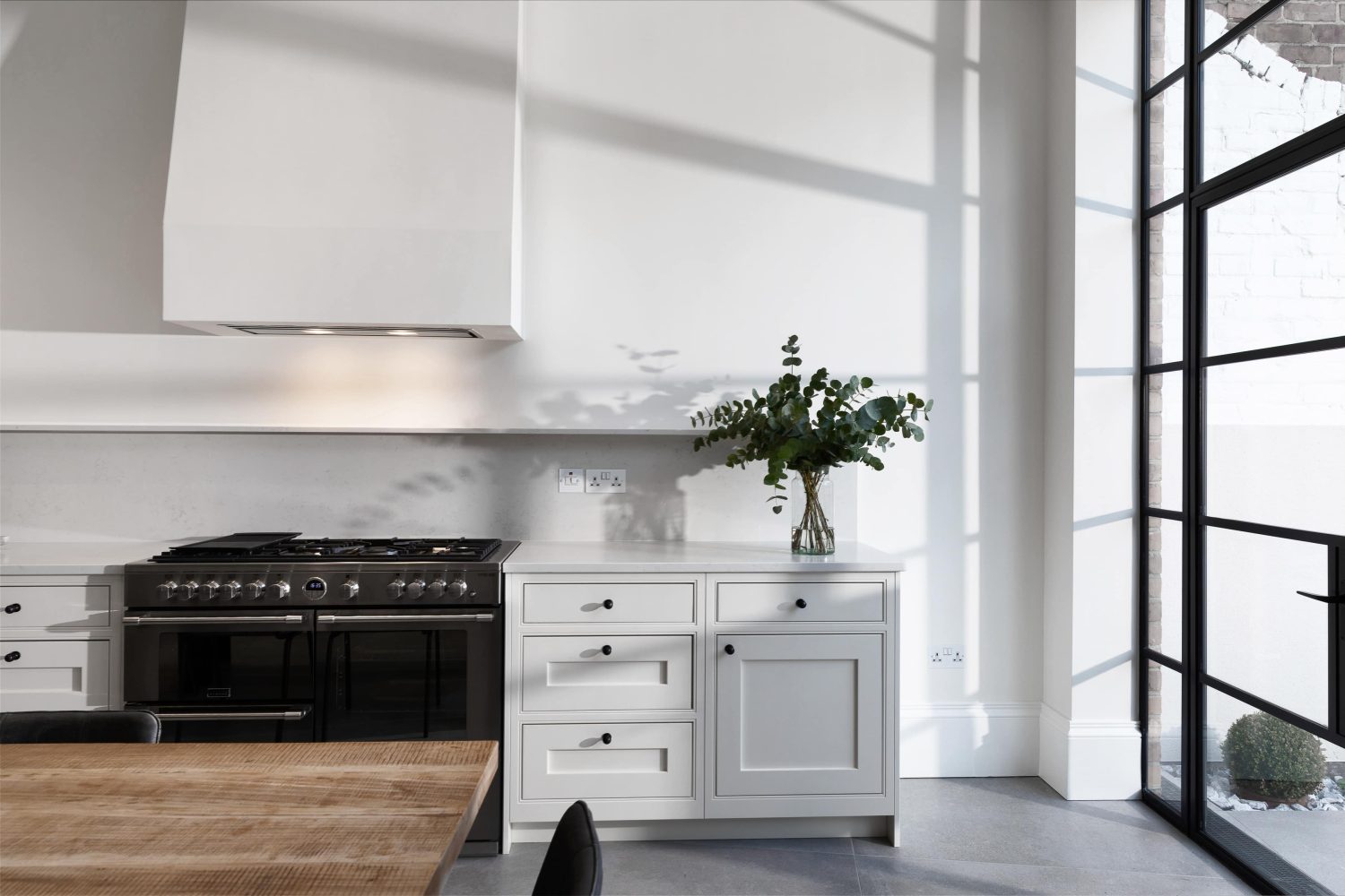 Kitchen with white walls and cabinets with a silver stove unit built in and leafy green plant on top of the counter
