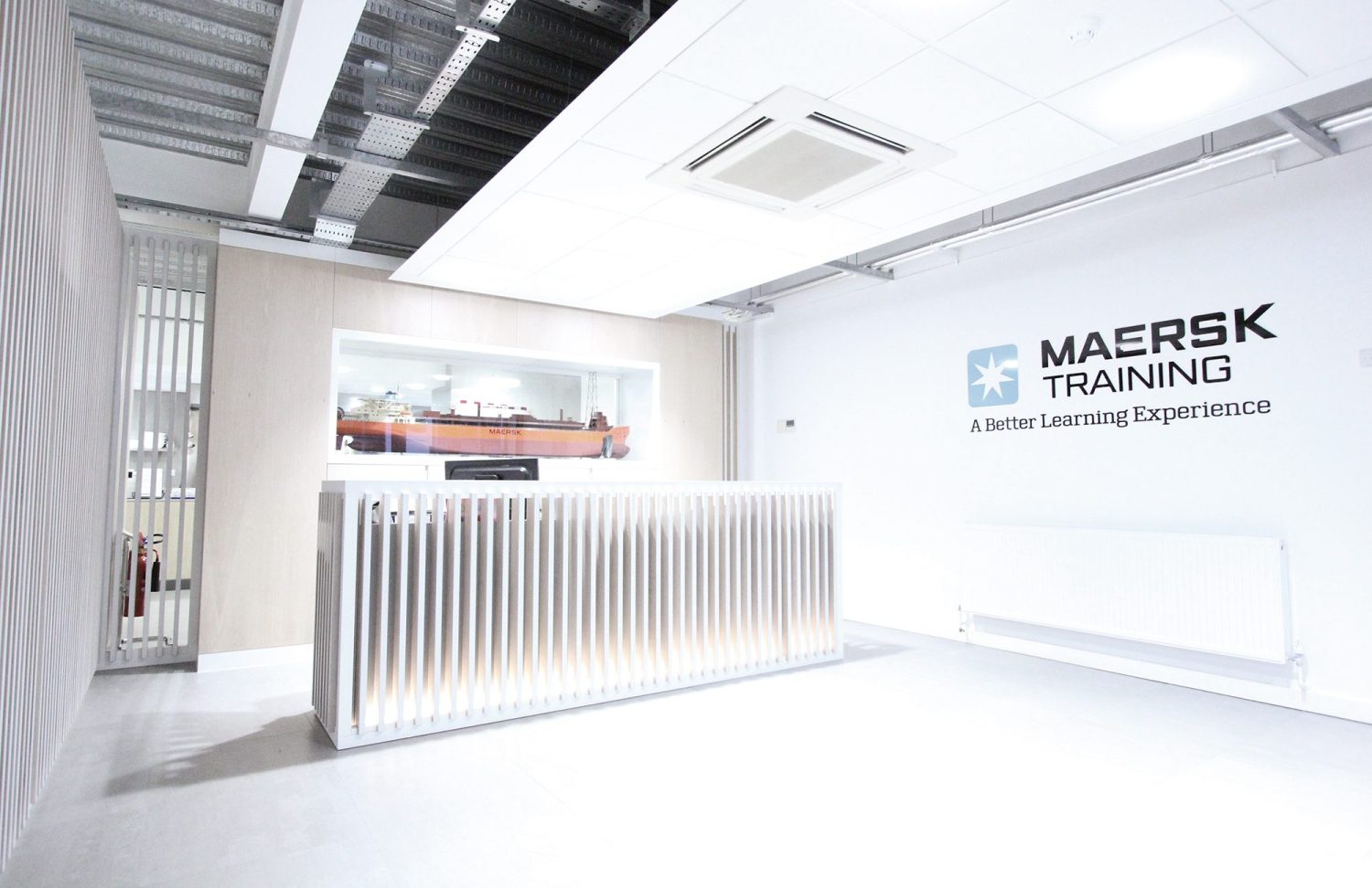 Reception desk with wall of wooden slats around, a model ship behind and company logo graphic on the wall to the right