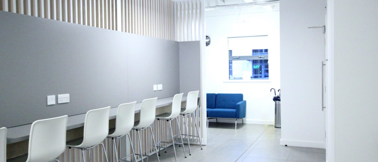Grey partition wall with a bench attached an white stools along it