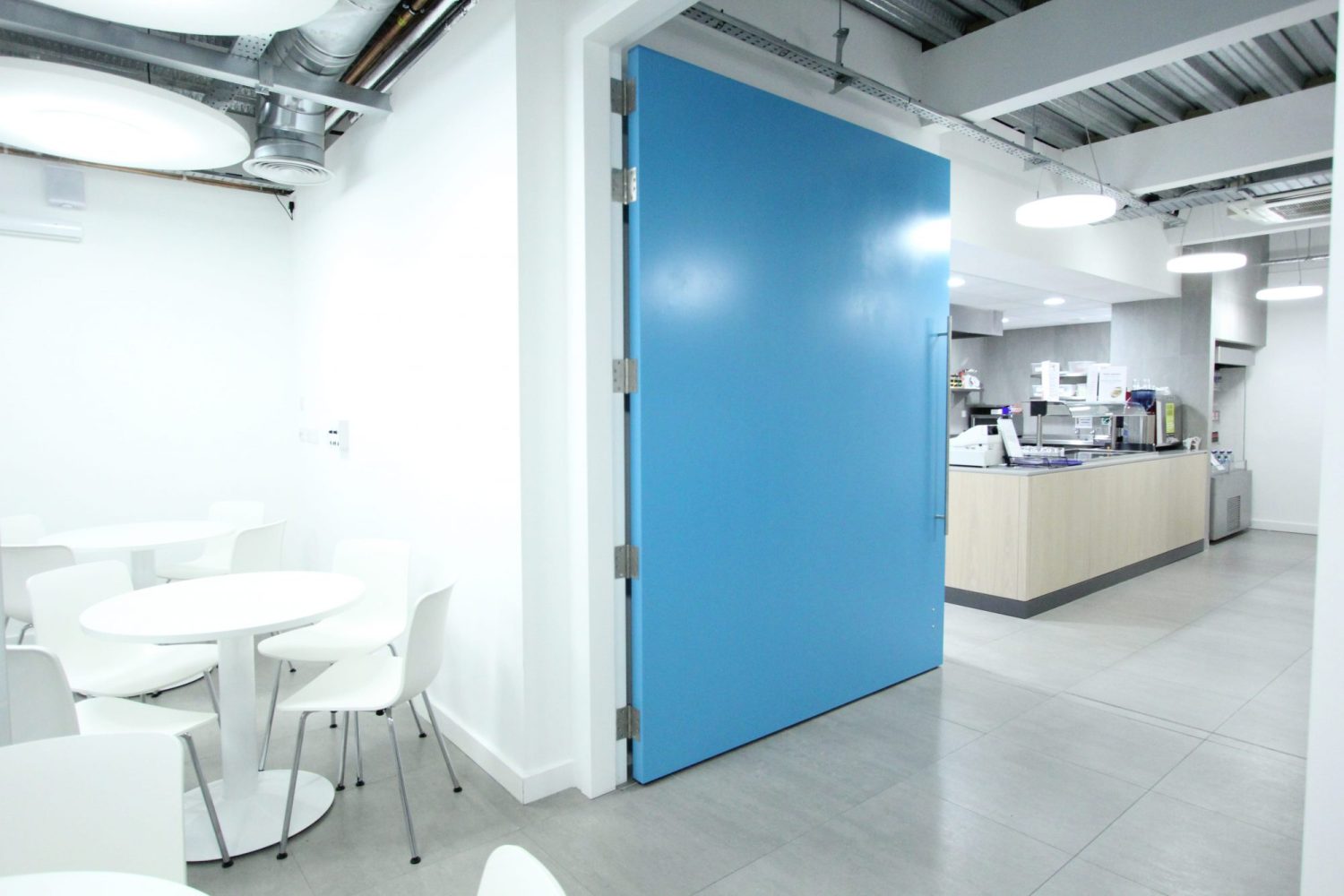 Large blue door open between a white seating area and canteen counter