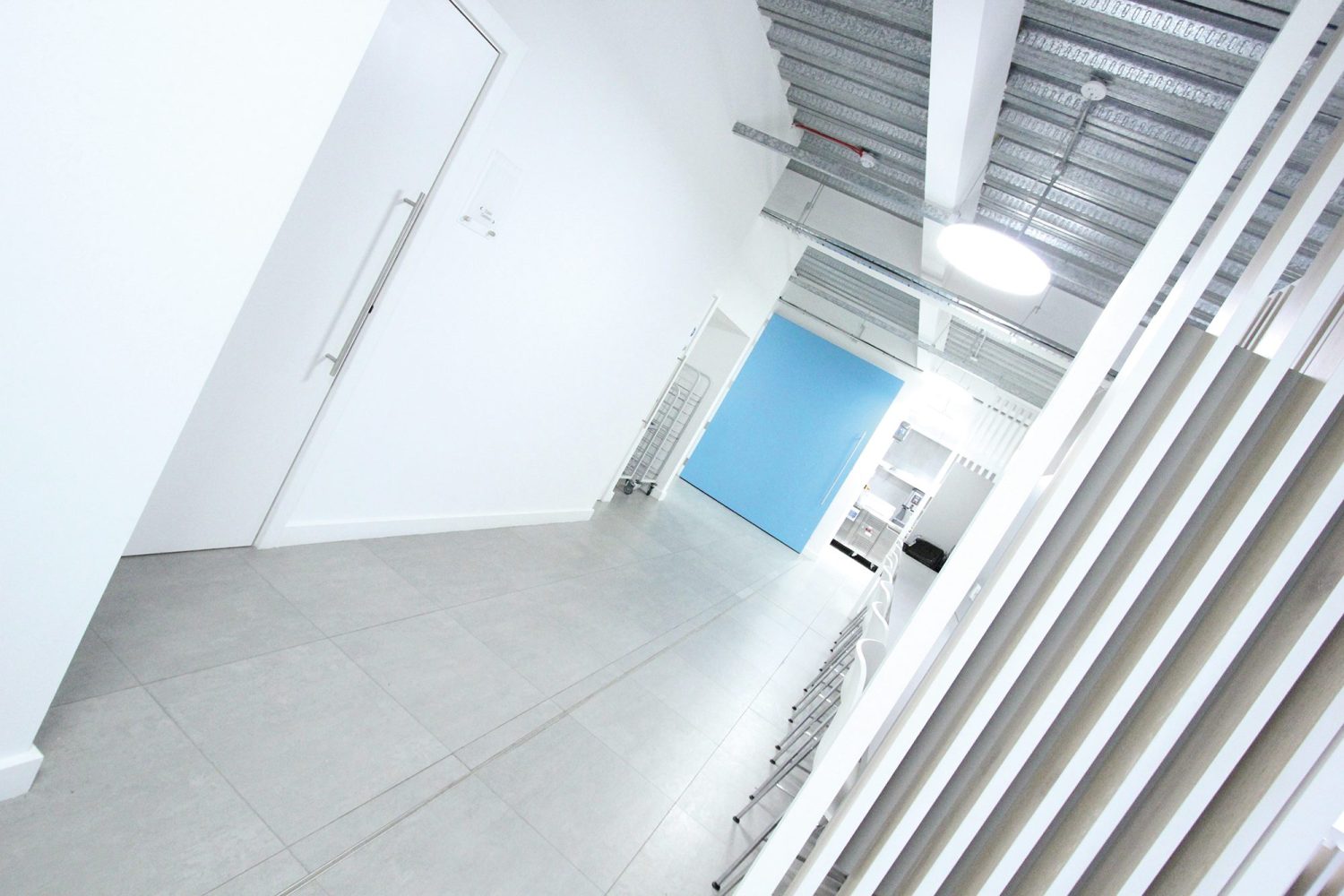 White corridor with large blue door at the end and white seating area to the right