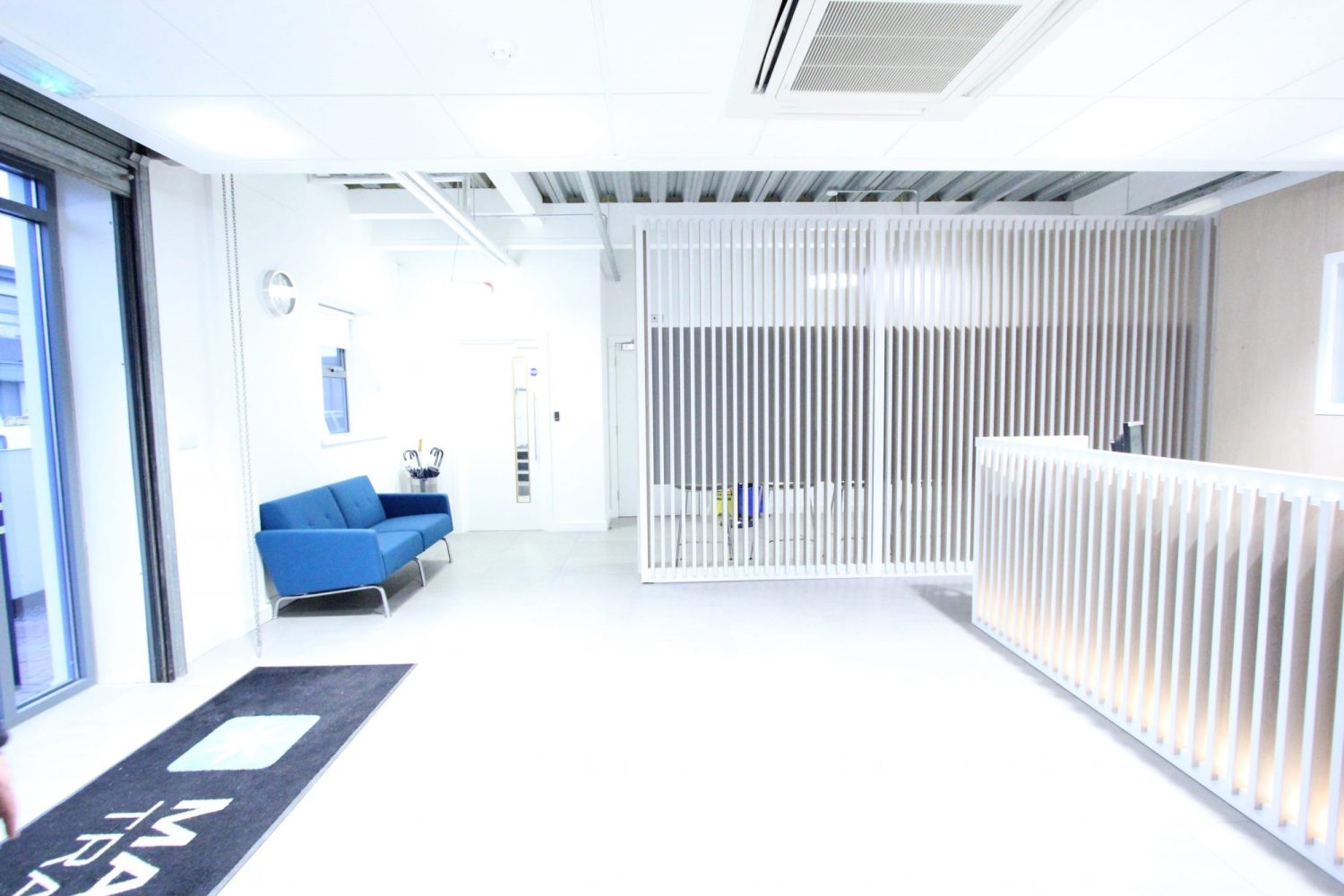Reception area with a blue sofa to the left and partition walls made of wooden slats around reception desk