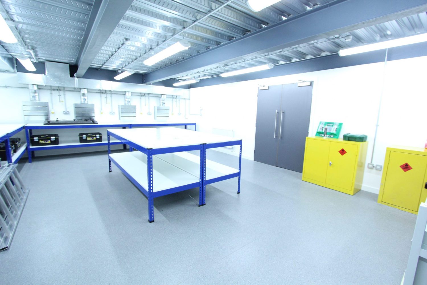 Room with a blue table in the centre with grey double doors and bright yellow containers to the right