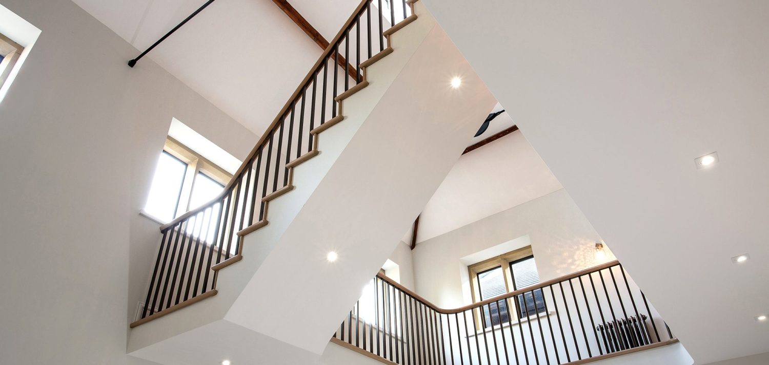 View of underside of a staircase in a large home with white walls and wooden balustrade