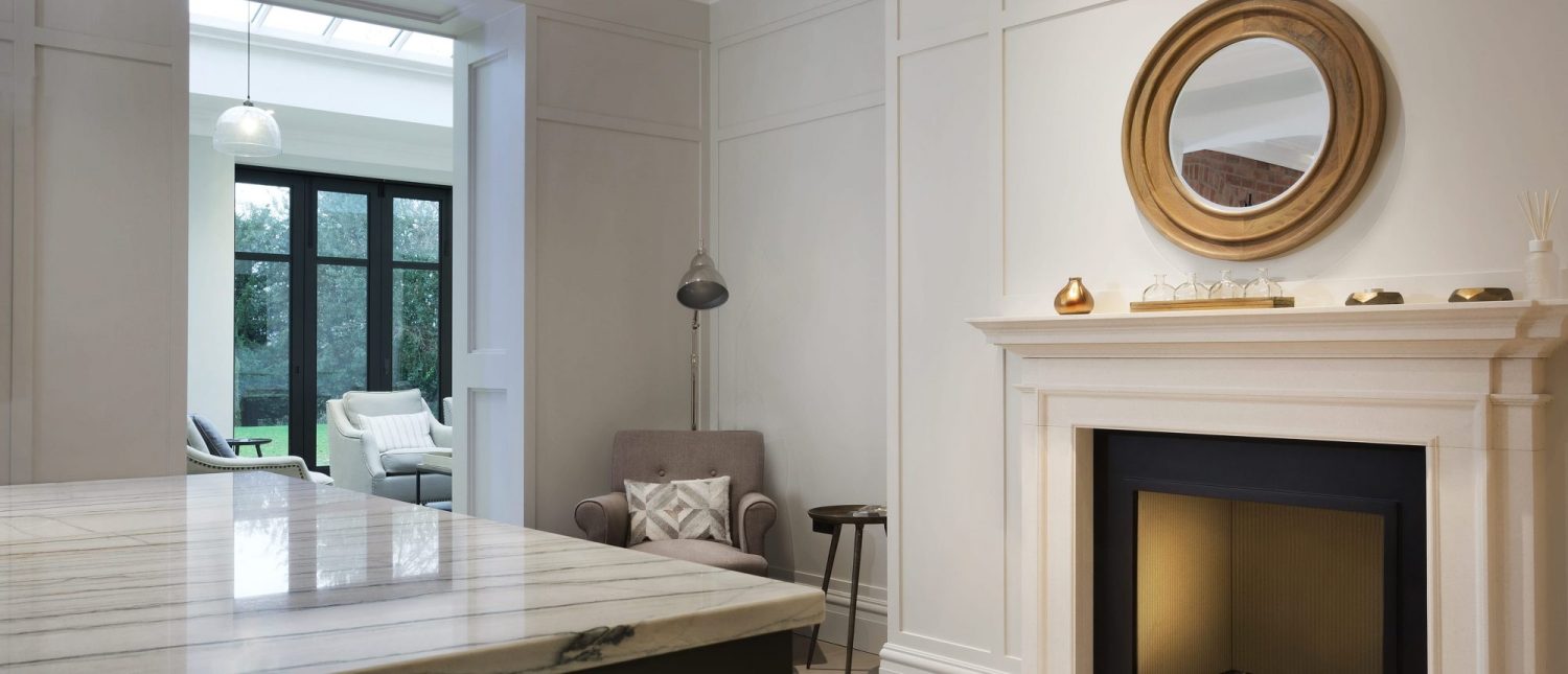 Living space with grey chair in a corner and white and gold fireplace with gold mirror above