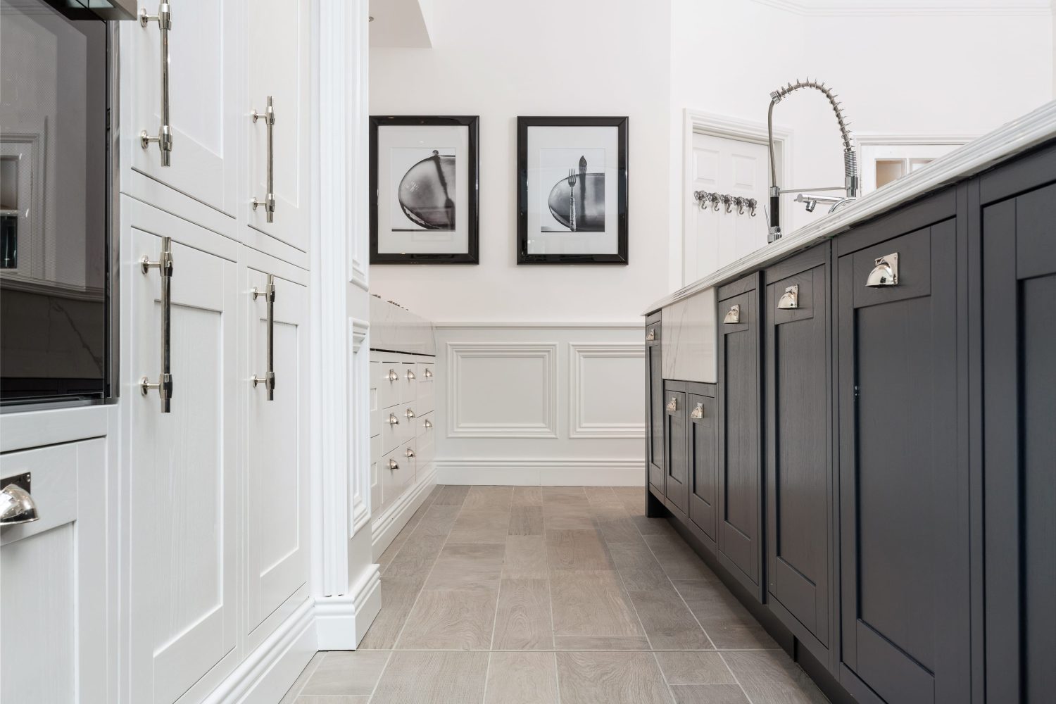 White kitchen cabinets on the left and dark grey cabinets of a kitchen island to the right with framed images on the far wall