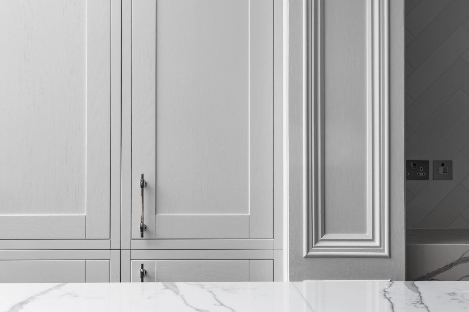 Close up white cabinet door with a silver handle and molding on wall to the right