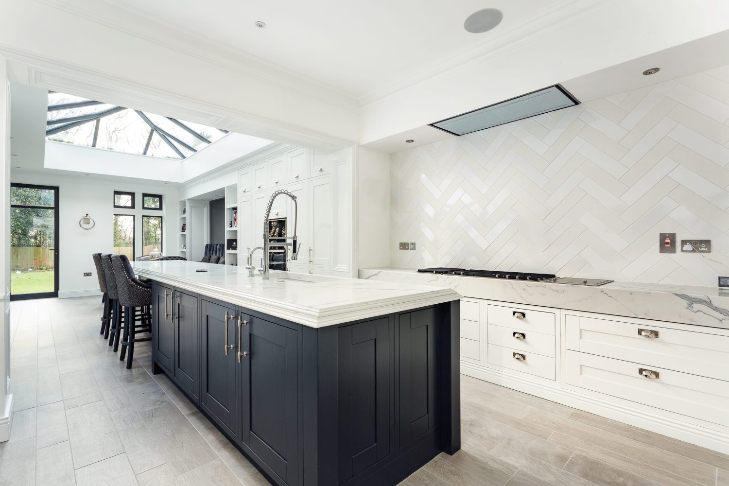 Kitchen with off-white tiled wall above white drawers and a large dark grey island with white marble countertop