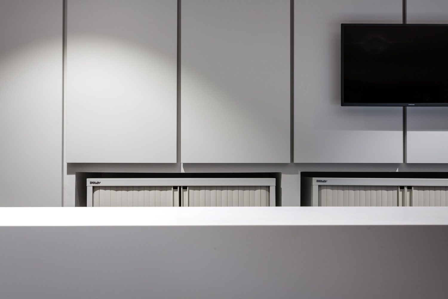 White panelled wall with TV to the right and cabinets beneath