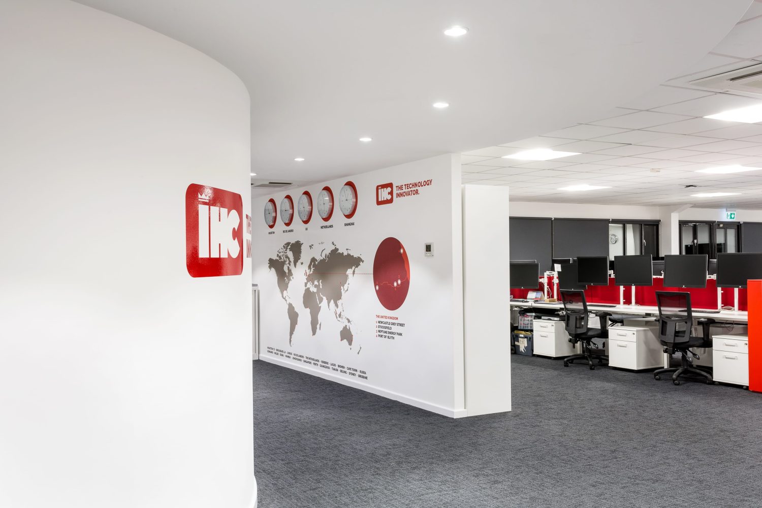 White wall with large map graphic and office area to the right with red partition walls between desks