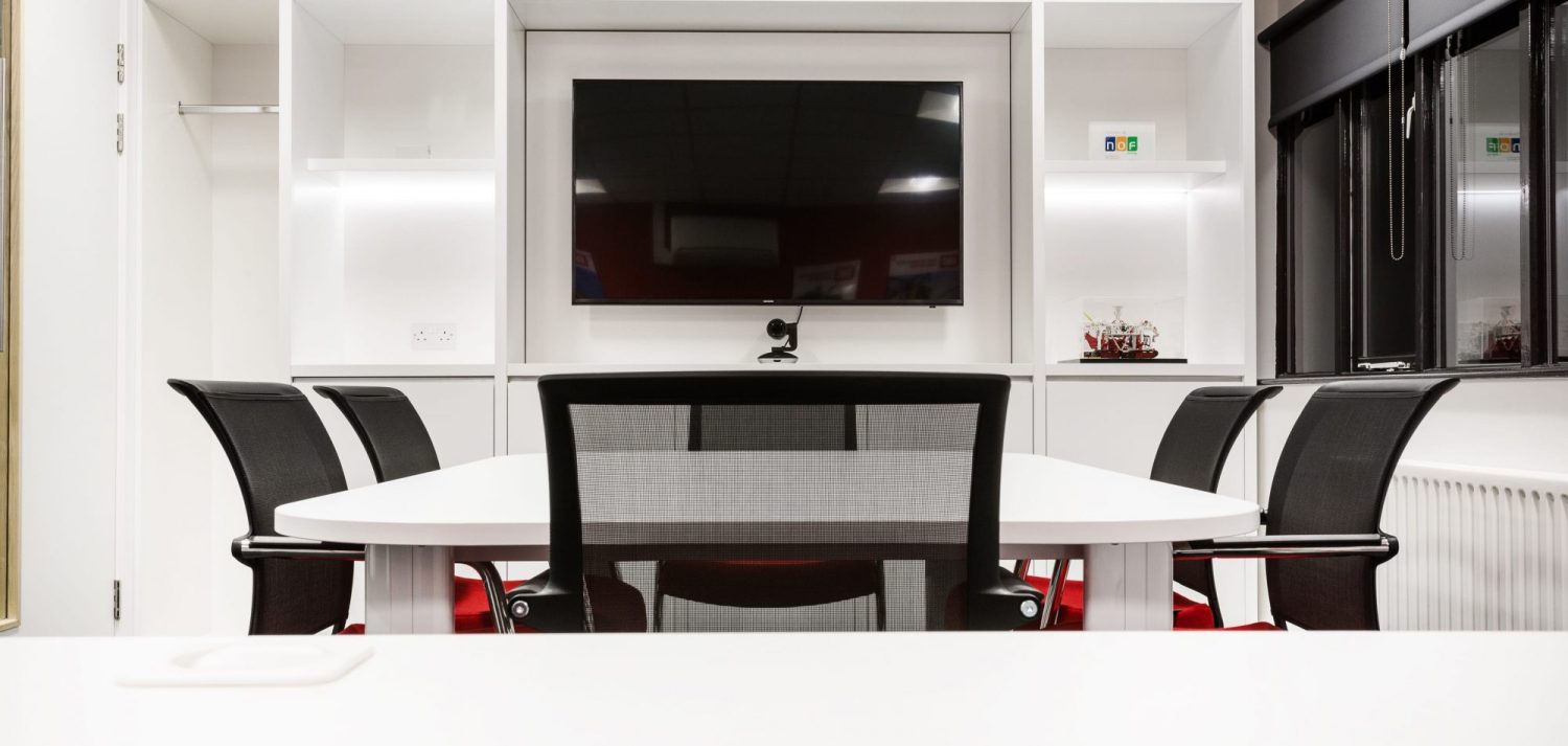 Meeting room with white table and black chairs in the centre with a TV on the wall
