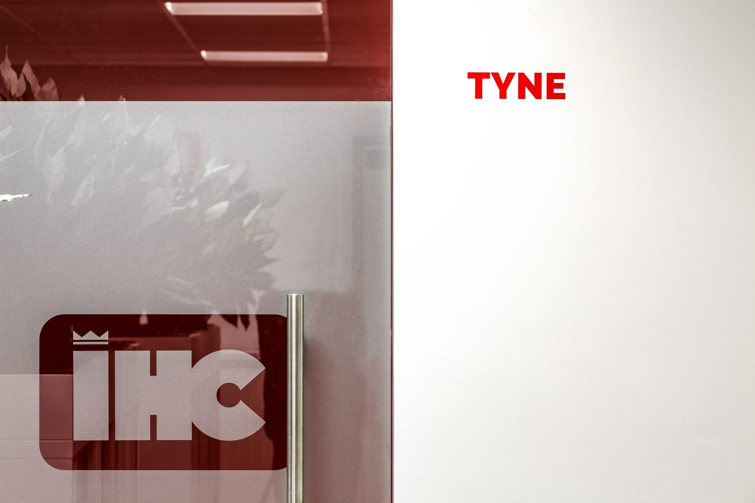 Glass door with metal handle and frosting with logo cut out. White wall with graphic to the right