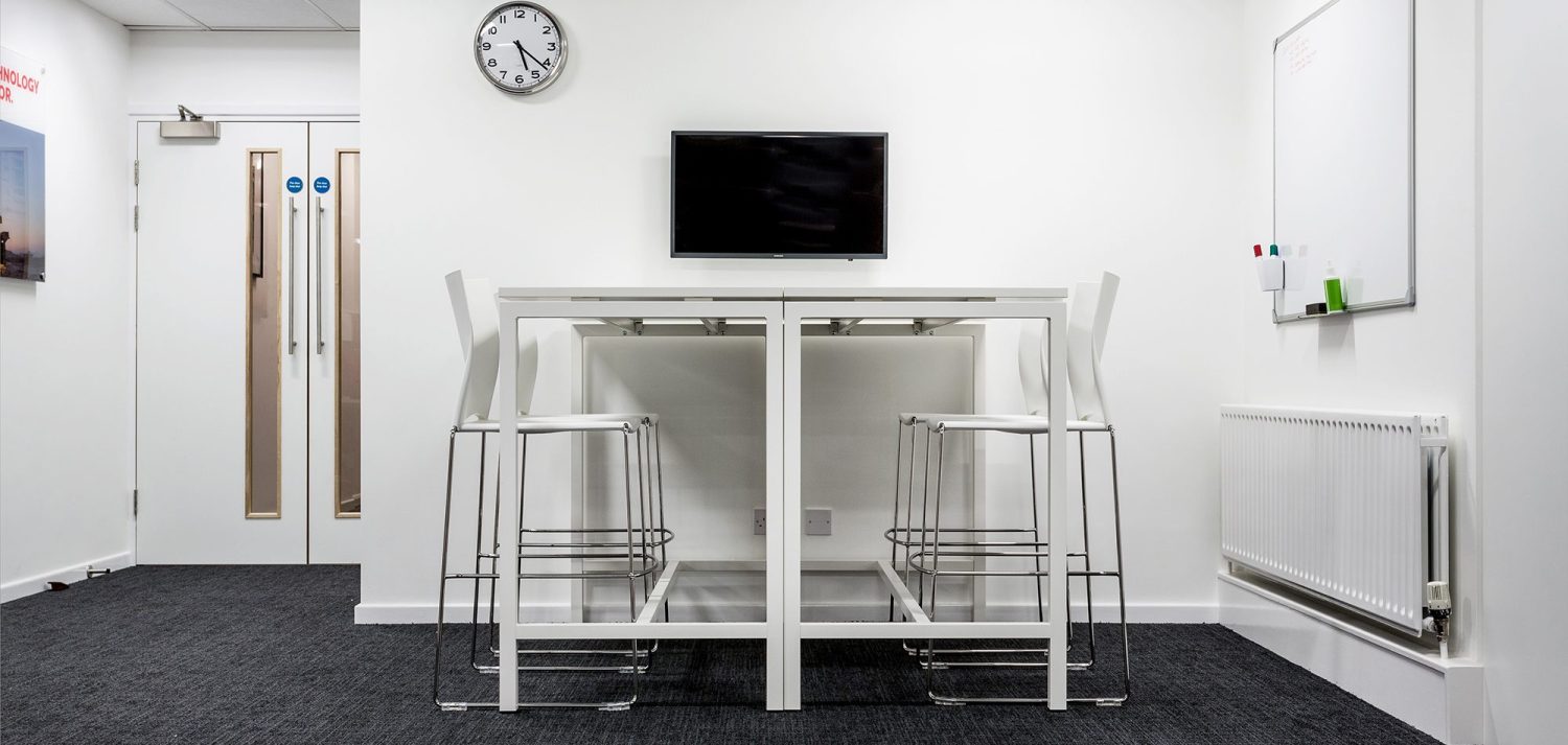 White table with white stools and a small TV and whiteboard on the walls beside