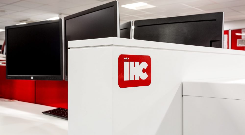 White partition wall to the side of desks with monitors on top and red partitions between desks