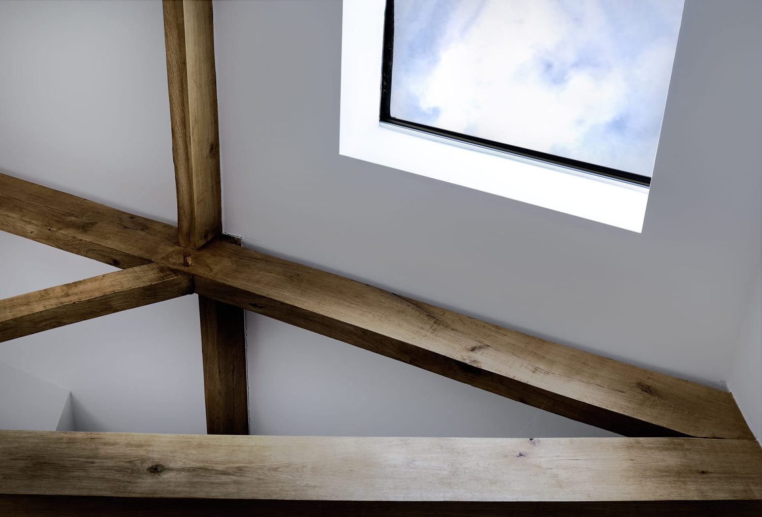 Skylight in white ceiling with wooden beams across ceiling