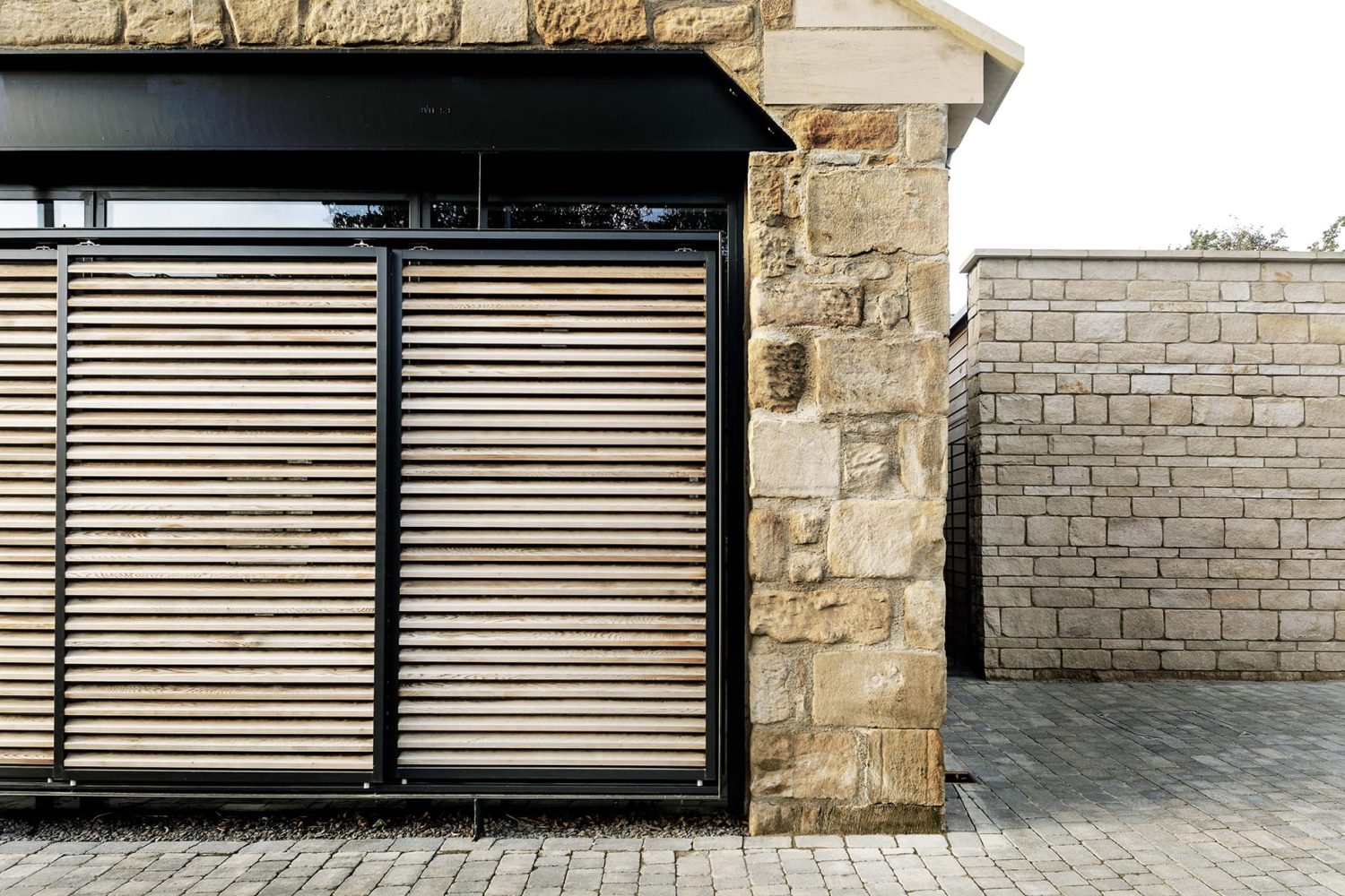 Corner of barn conversion exterior with stone walls and wooden shutters over black framed windows