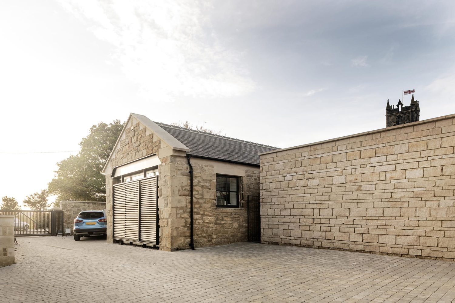 Exterior of barn conversion with stone walls and church behind wall