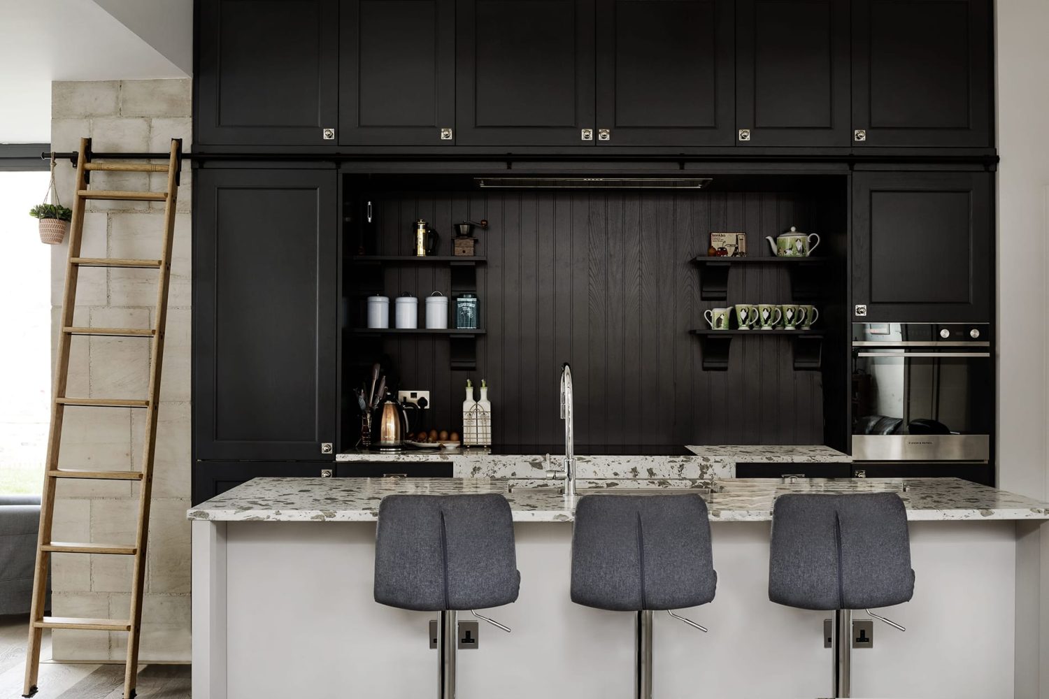 Kitchen with black cabinets and library ladder to the side with island in front with white stone countertop