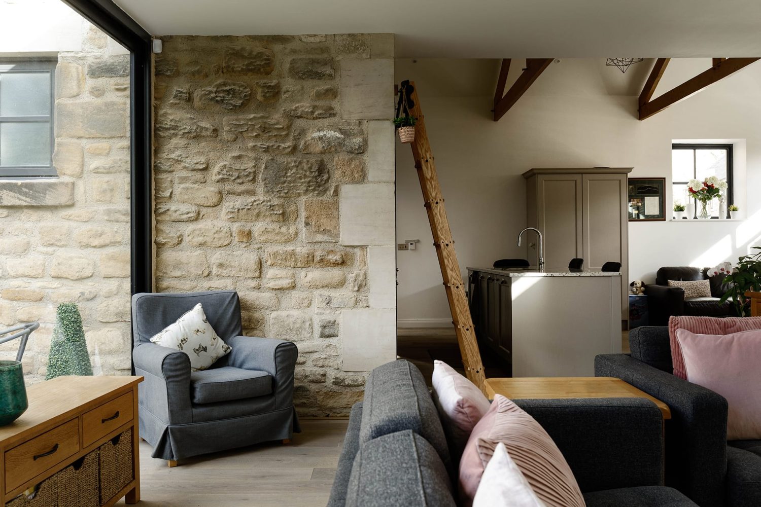 View of kitchen library ladder and grey island from living room with grey sofas and pink cushions