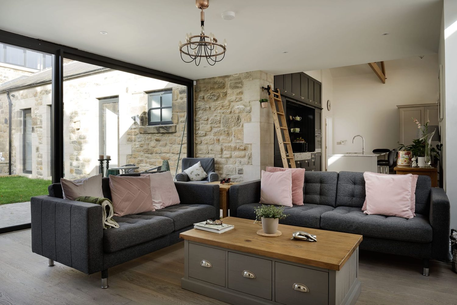 Living room with grey sofas with pink cushions and grey coffee table in centre with wooden top
