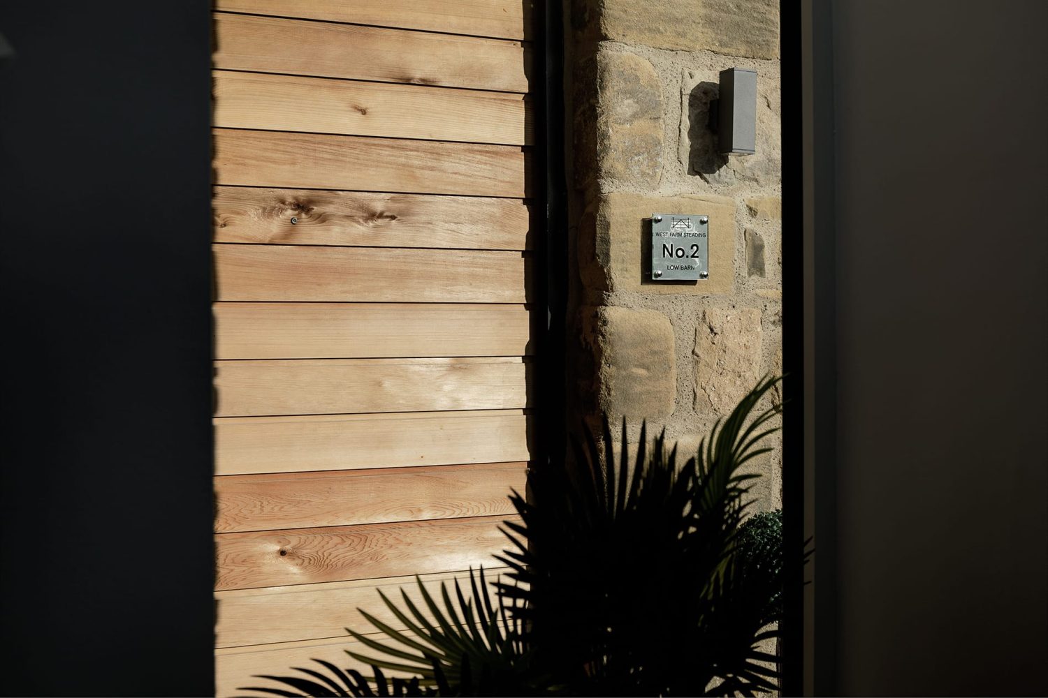 Wooden panelled wall connecting to exposed stone wall with leafy plant below
