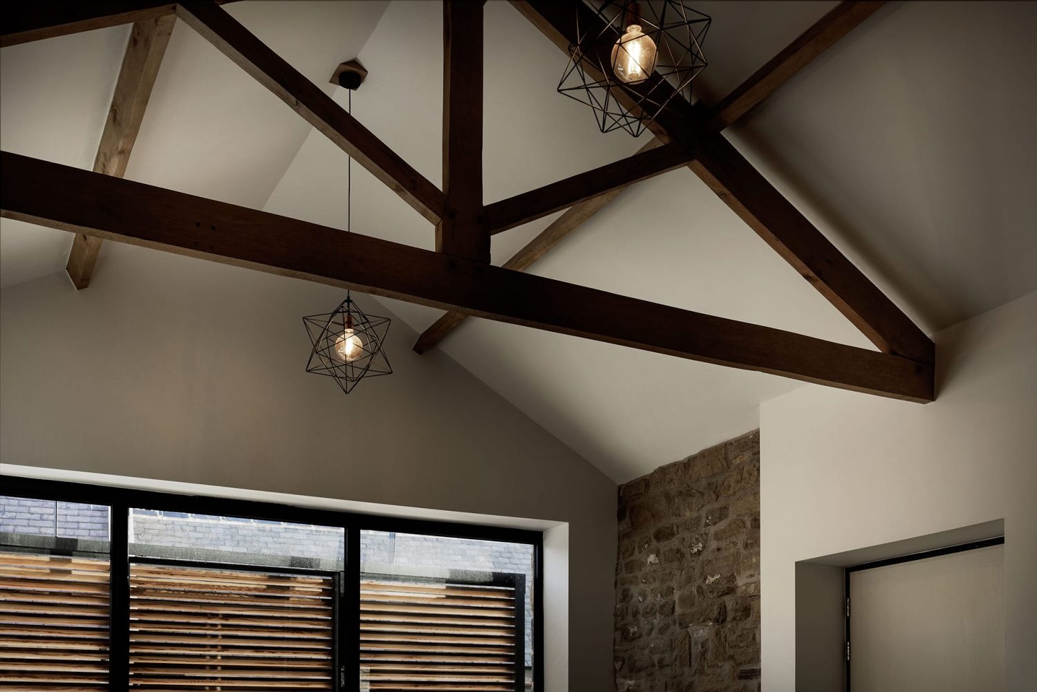Pointed ceiling with wooden beams across and geometric pendant lamps with exposed lightbulbs hanging