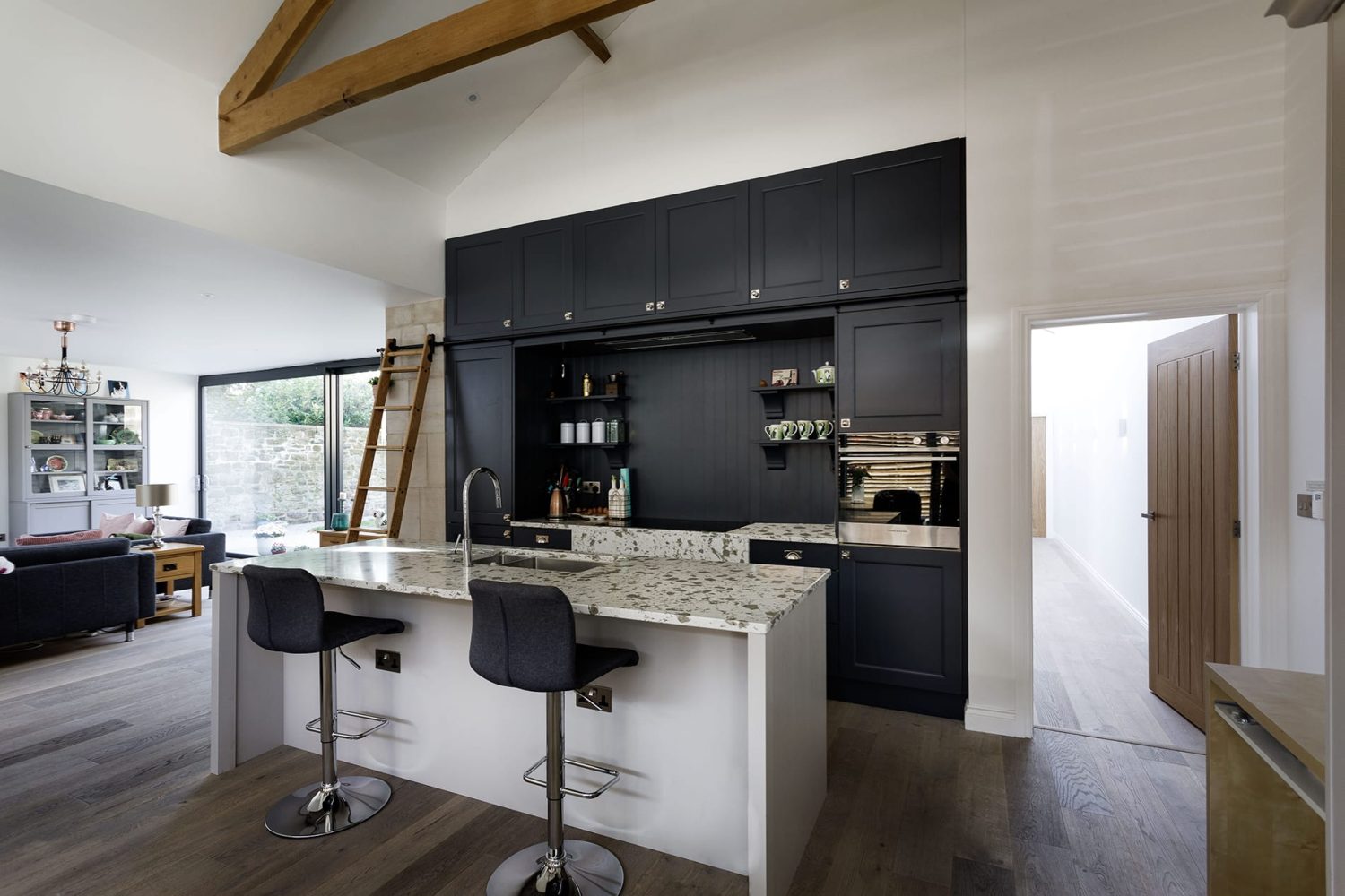 Kitchen with black cabinets and an island with white and grey stone countertop and library ladder to the left