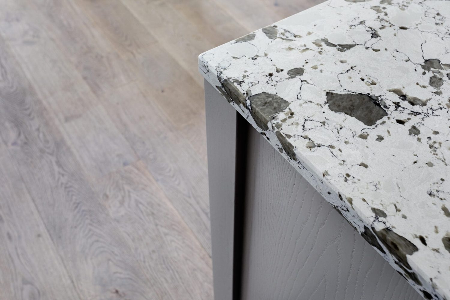 Close up corner of kitchen island with grey sides and a white and grey stone countertop against a wooden floor
