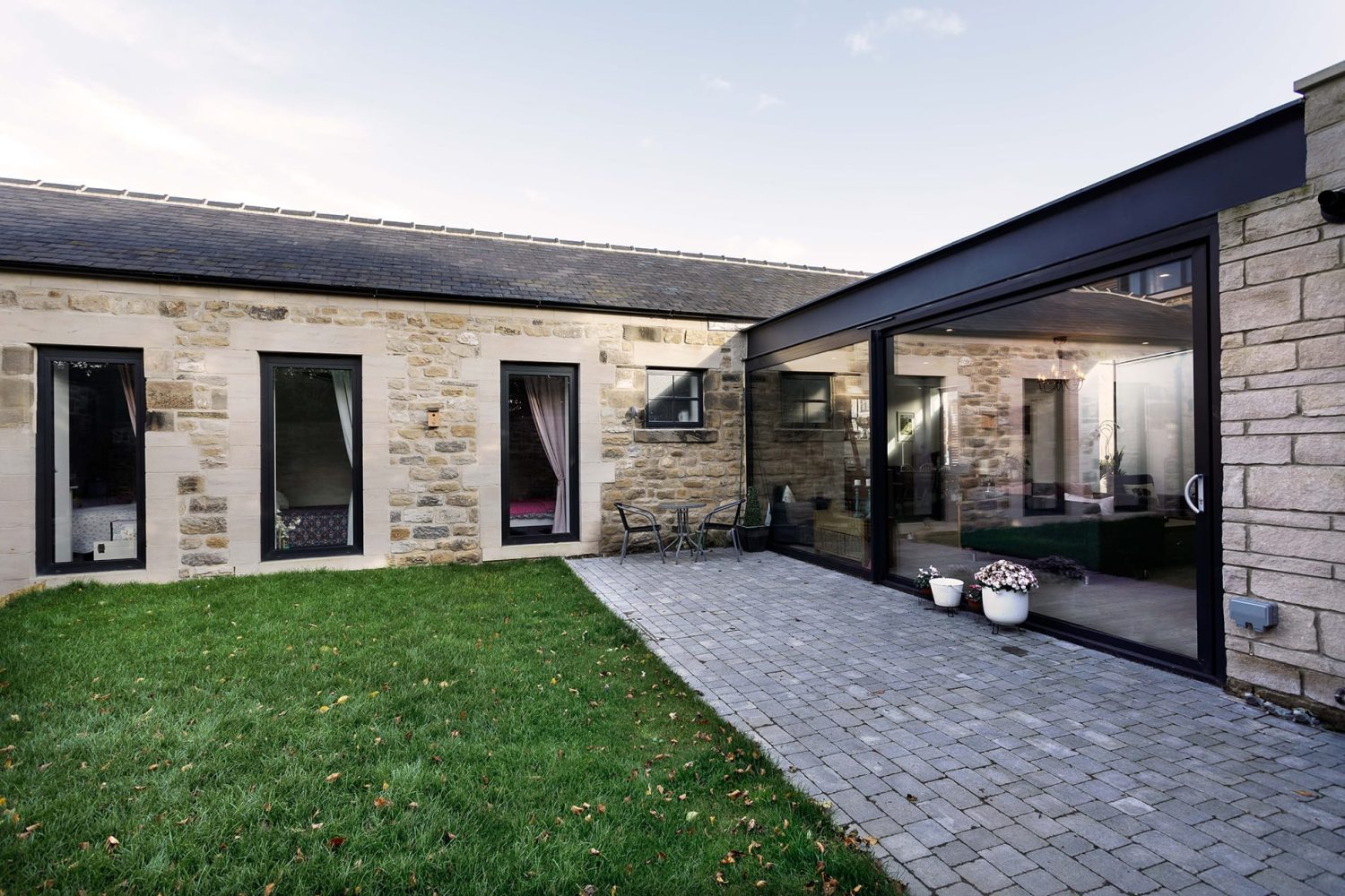 Exterior of barn conversion with stone walls and large glass sliding doors and windows with black frames