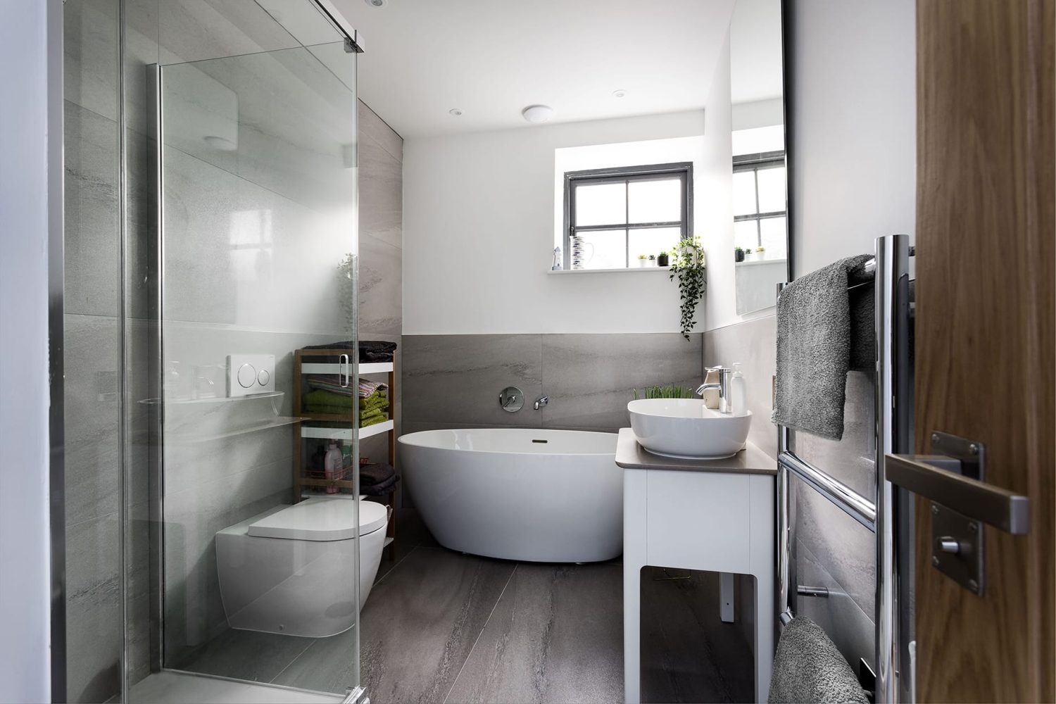 Bathroom with grey tiles and large white bath beside white sink and toilet