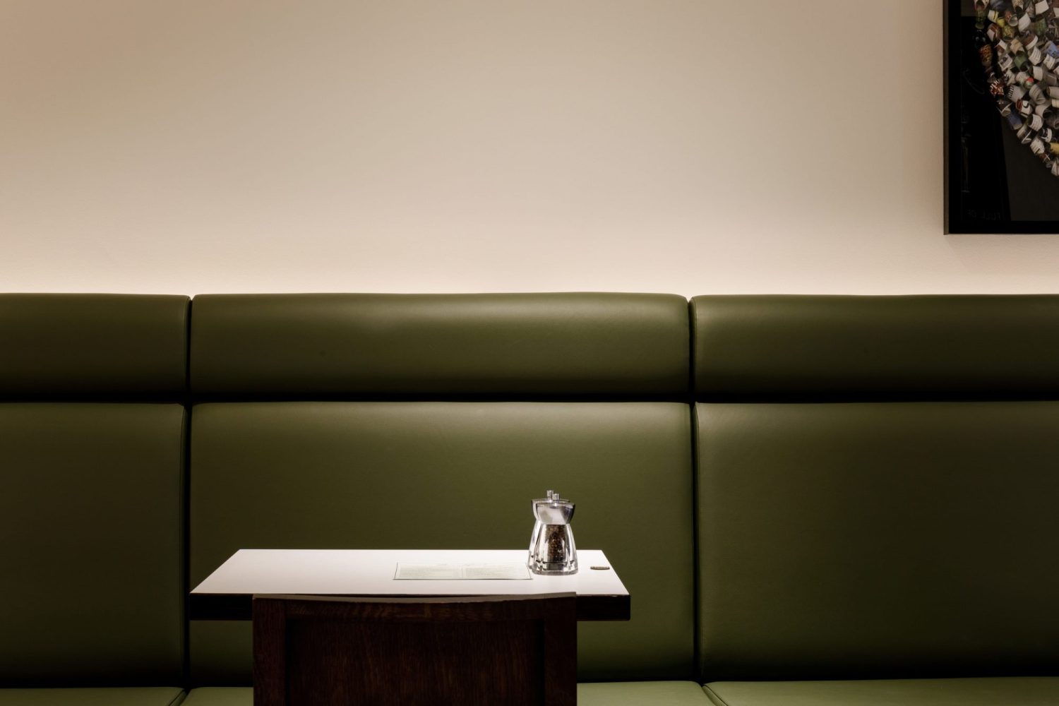 Green leather booth seat along a white wall with small square table in the centre and wooden chair