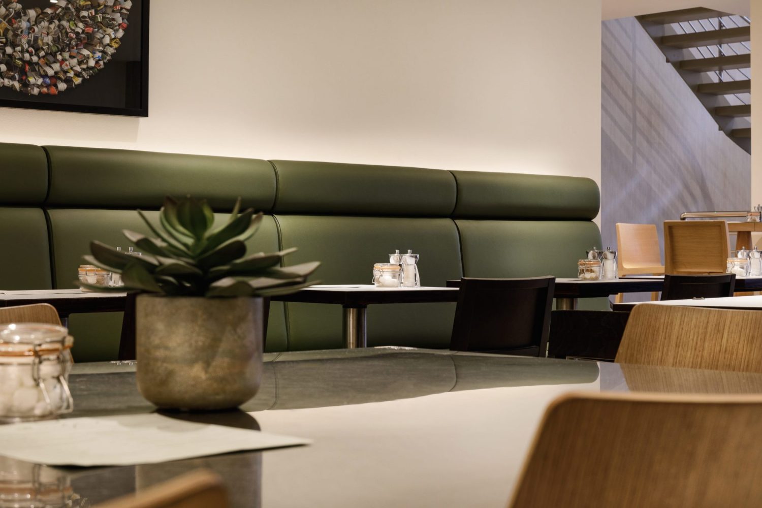 Green leather booth seat along wall with black tables and chairs