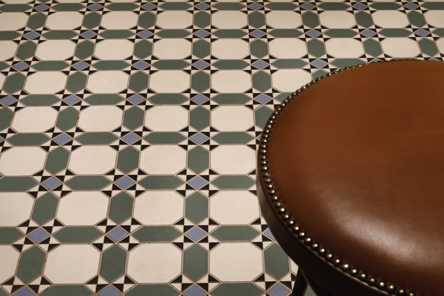 Green geometric pattern tiled floor with a brown leather stool to the right