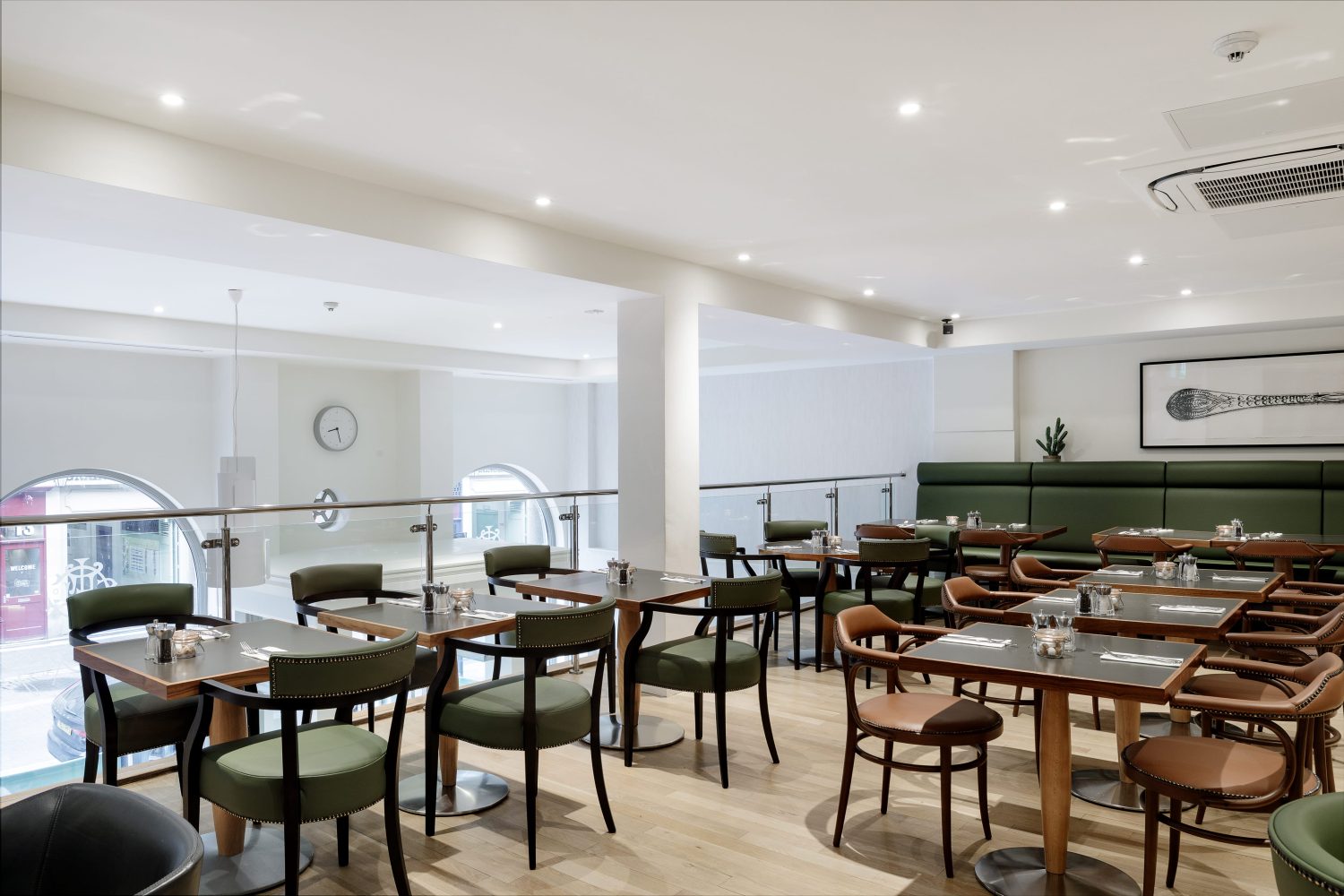 Cafe seating area on a raised floor with a glass barrier. Green and brown leather chairs with square tables in rows