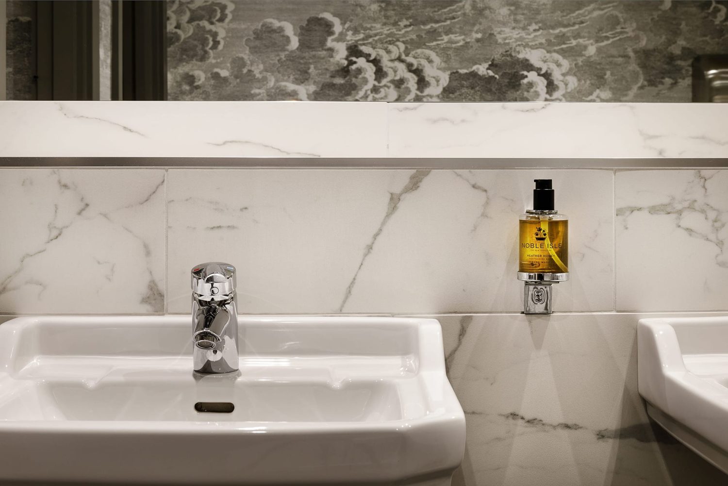 White bathroom sink with a chrome tap and sink holder attached to white marble wall