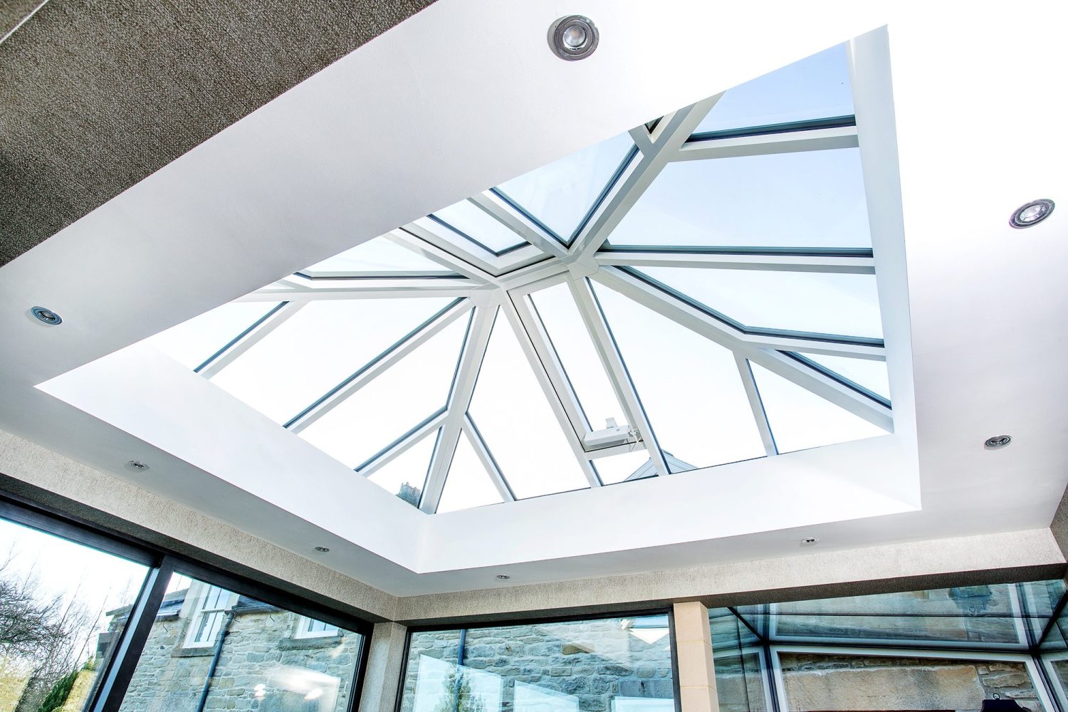Glazed ceiling of extension with white window frames and spotlights surrounding