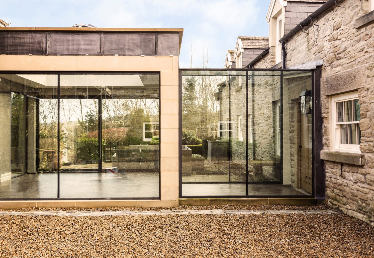 Exterior view of extension with glazed walls attached to house with exposed stone walls
