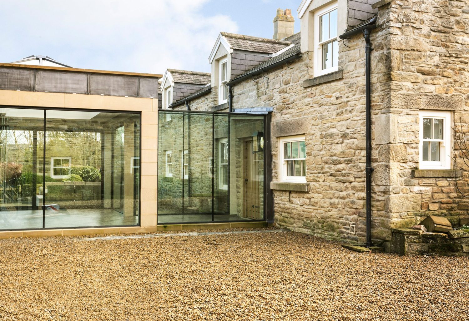 Exterior of extension with glazed walls attached to exposed stone building with white windows